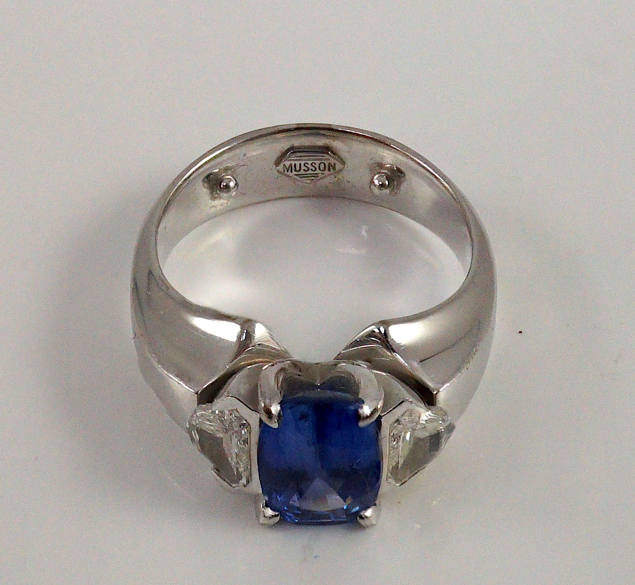 A modern white gold (tests as 18ct), single stone oval cut Ceylon sapphire and two stone shield cut diamond set dress ring, by Musson